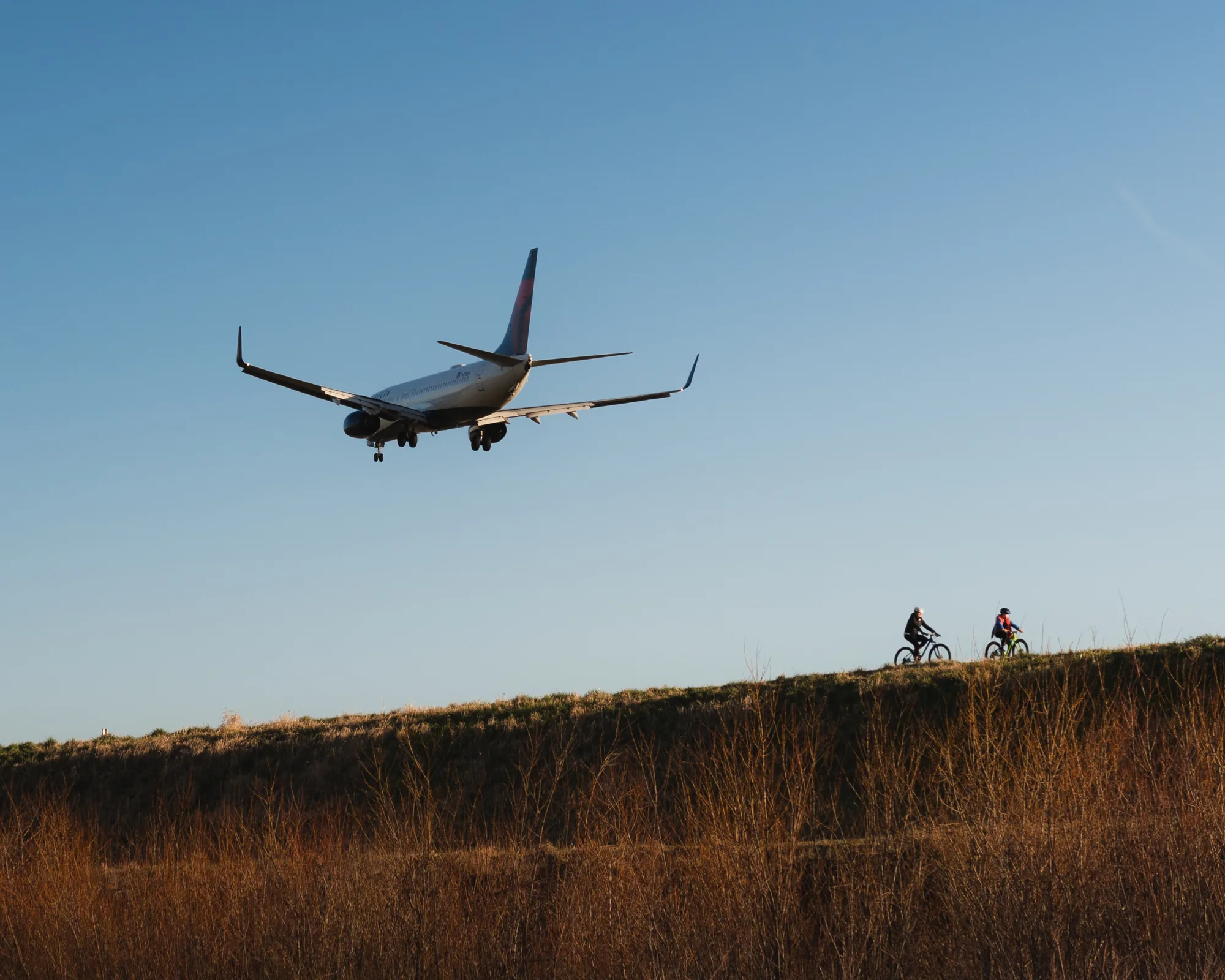 A passenger jet on approach over two mountain bikers on a ridge at golden hour