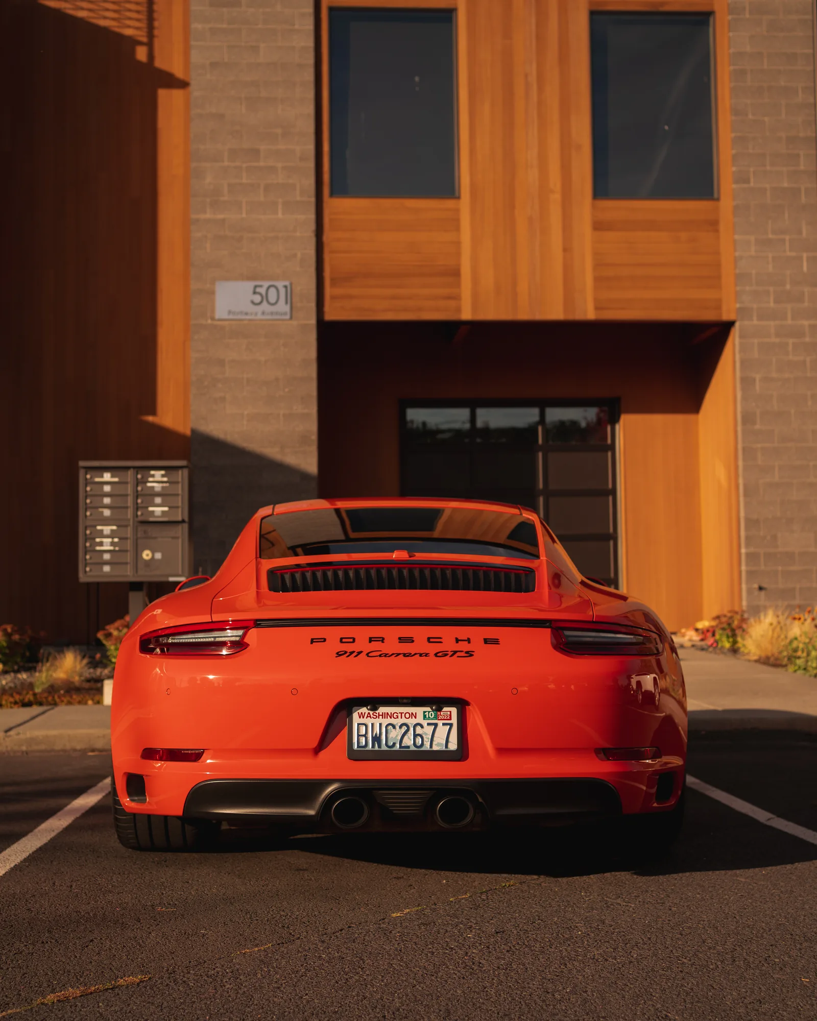 Rear view of an orange Porsche 911 Carrera GTS parked in front of a wood and brick building